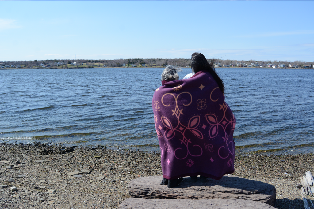 Photo of two individuals with a purple blanket, looking out onto the water 